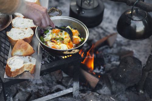Detail view of camp fire cooking, breads are in a row, a tea pot and egg pan is on the fire with copy space